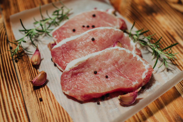 Rauw varkensvlees biefstuk op een donkere houten tafel met rozemarijn en knoflook - Foto, afbeelding