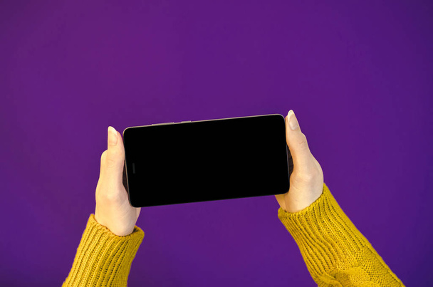 Mujer manos suéter amarillo usando el teléfono celular que sostiene el teléfono móvil inteligente con pantalla oled en el color ultravioleta del fondo del año. Close up Flat Lay bussines composición Vista superior
  - Foto, Imagen
