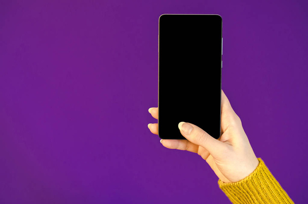Vrouw handen gele trui met behulp van de mobiele telefoon bedrijf slimme mobiele telefoon met oled-display op ultra violet kleur van de achtergrond van het jaar. Close-up van plat leggen bussines samenstelling bovenaanzicht  - Foto, afbeelding