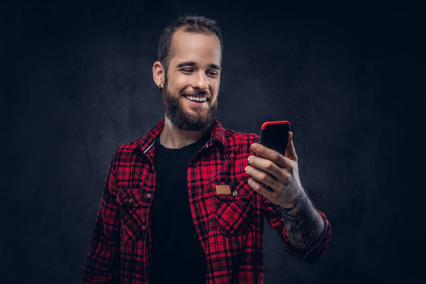 Egy szakállas csípő ember mosolyogva és nevetve olvasat text üzenetek a smartphone. - Fotó, kép