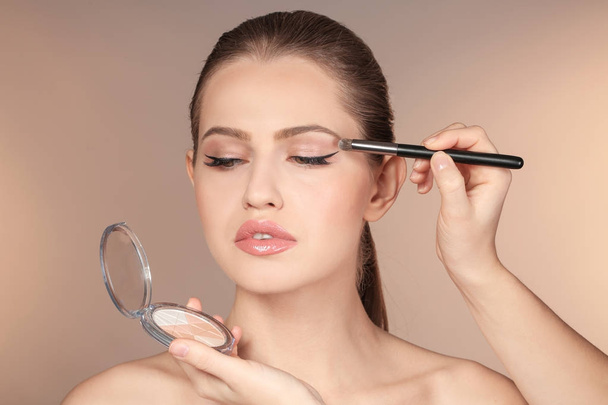 Professional visage artist applying makeup on woman's face on color background - 写真・画像