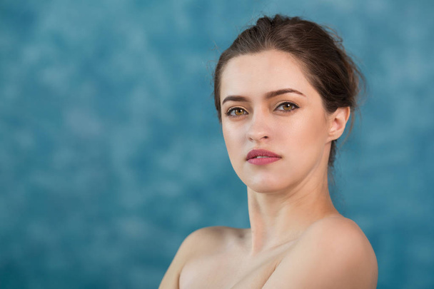 Young attractive girl with black hair fixed behind, big eyes, thick eyebrows and naked shoulders holding hand near face at gray background, portrait, copy space. - Valokuva, kuva