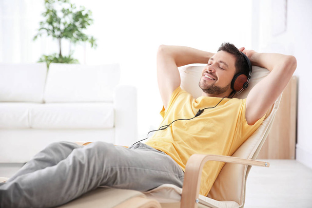 Young man listening to music while relaxing in armchair at home - Photo, Image