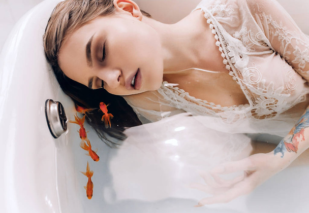 Mujer joven tiene relajarse en la bañera con agua y la natación peces de colores. Primer plano.
. - Foto, imagen