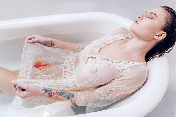 Žena si relaxovat ve vaně s vodou a plavání goldfishes v její lem šatů. - Fotografie, Obrázek