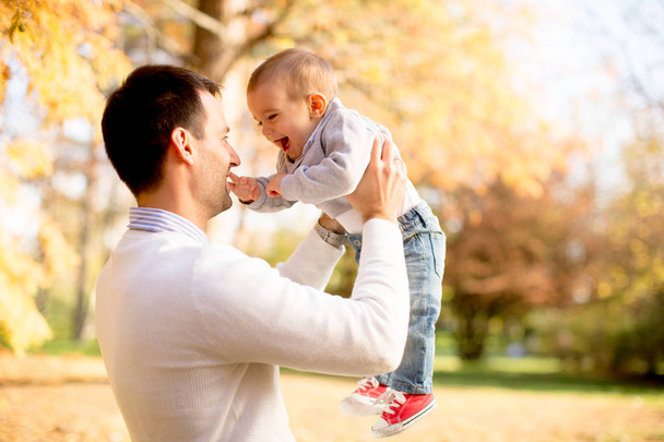 Fiatal apa, és a baba fiú játék őszi parkban a napsütéses napon - Fotó, kép