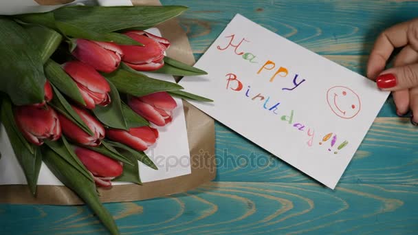 Το Top view χαρούμενα γενέθλια μήνυμα Σημείωση και τουλίπες μπουκέτο με λουλούδια σε ένα ξύλινο τραπέζι. Έννοια σχέση αγάπης. Γενέθλια έννοια. Πυροβόλησε σε ανάλυση 4 k - Πλάνα, βίντεο