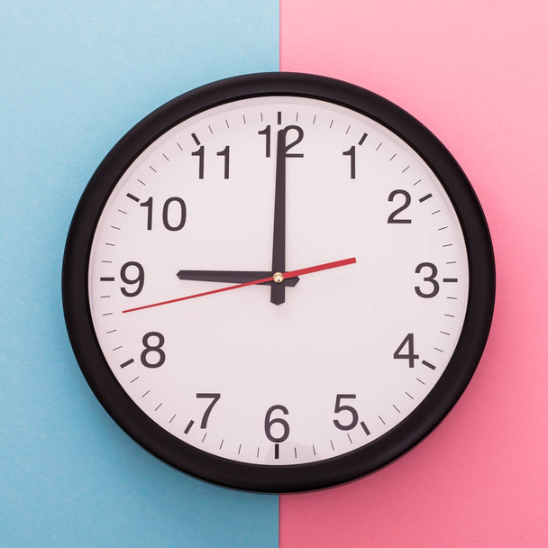 Relógio de parede grande isolado em fundo azul e rosa. Nove horas.
. - Foto, Imagem