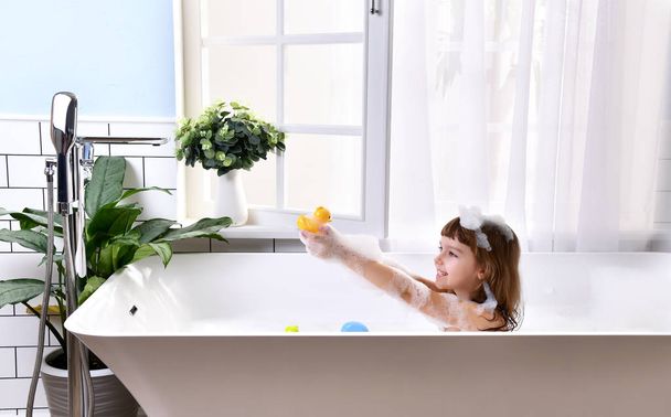  Happy little baby girl sitting in bath tub playing with duck toys  in the bathroom - Zdjęcie, obraz