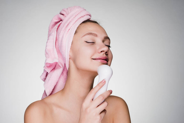 happy woman with a towel on her head cleans the skin of her face with a brush for deep cleaning - Foto, Bild