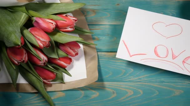 Widok z góry miłości wiadomości Uwaga i bukiet kwiatów tulipany na drewnianym stole. Koncepcja relacji miłości. Saint Walentynki. Strzał w 4 k - Materiał filmowy, wideo