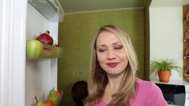 A woman is eating a red apple at home in the kitchen. - Filmati, video