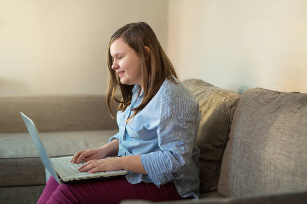 beautiful teenage girl full body working behind laptop at home on couch - Foto, Imagem