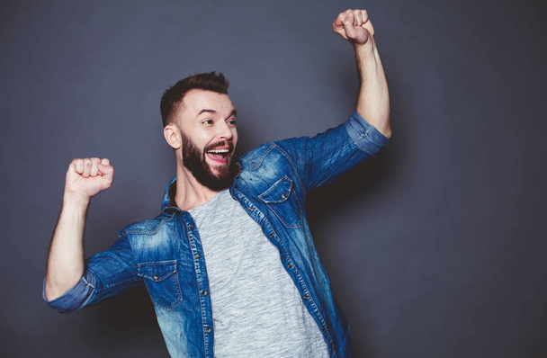 This is cool news. Cheerful and joyful bearded man in a denim shirt on a gray background. - 写真・画像