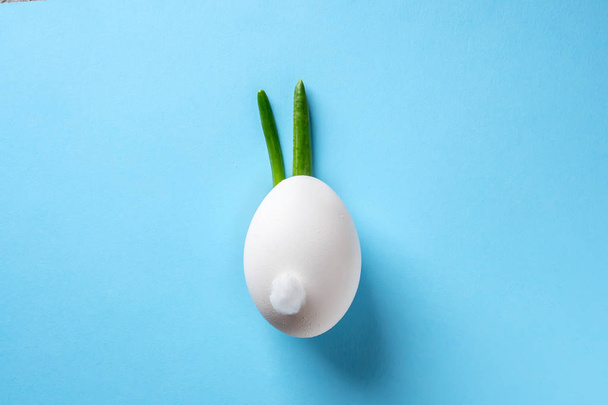 Egg shell and feathers green onion imitation rabbit bunny on blue colored paper background. Food concept minimal Easter - Фото, изображение