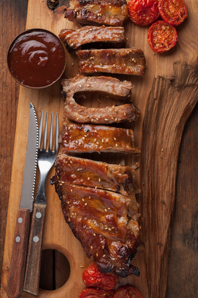 Pork ribs in barbecue sauce and honey roasted tomatoes on a wooden board. A great snack to beer on a rustic wooden table. Top view - Фото, зображення