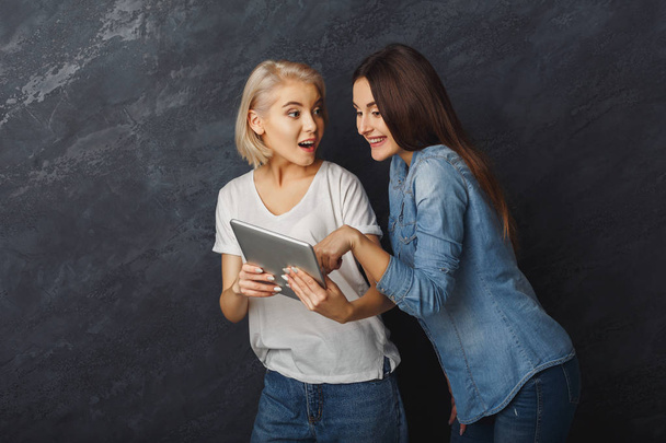 Neugierige Freundinnen mit Tablet vor dunklem Studiohintergrund - Foto, Bild