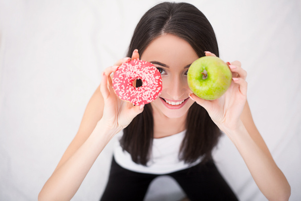 Diéta koncepció. Fiatal nő közötti választás gyümölcsök és édességek - Fotó, kép