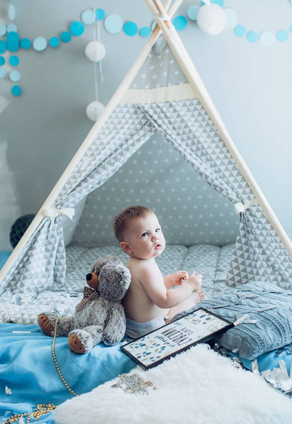 entzückender kleiner Junge posiert in der Nähe von Zelt mit Teddybär zu Hause - Foto, Bild