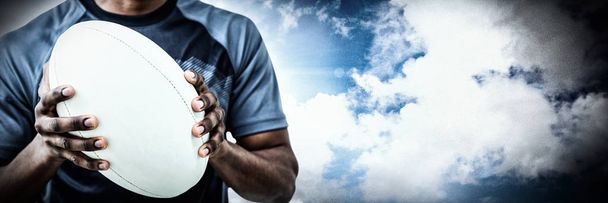 Mid section of sportsman holding rugby ball against spotlight in sky - Foto, Bild