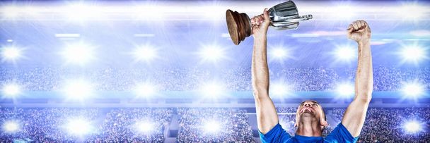 Happy rugby player holding trophy against digital image of crowded soccer stadium - Fotografie, Obrázek