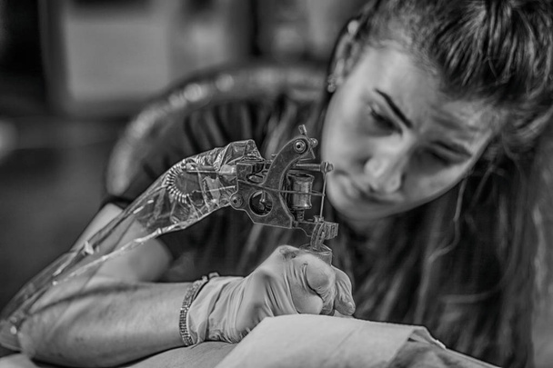 Tatuaggio dell'artista professionista sta tatuando la donna del corpo usando la macchina in uno studio di lavoro di design creativo
 - Foto, immagini