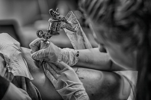 Κάνοντας επαγγελματίας καλλιτέχνης τατουάζ είναι τατουάζ γυναίκα σώμα χρησιμοποιώντας μηχανή σε ένα δημιουργικό έργο στούντιο σχεδιασμού - Φωτογραφία, εικόνα