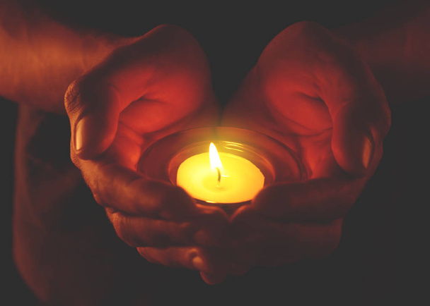 Nuori mies pitelee palavaa kynttilää pimeydessä
 - Valokuva, kuva