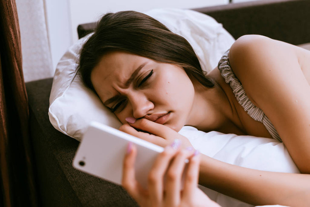 sleepy woman lies on the bed and looks into the phone - Foto, imagen