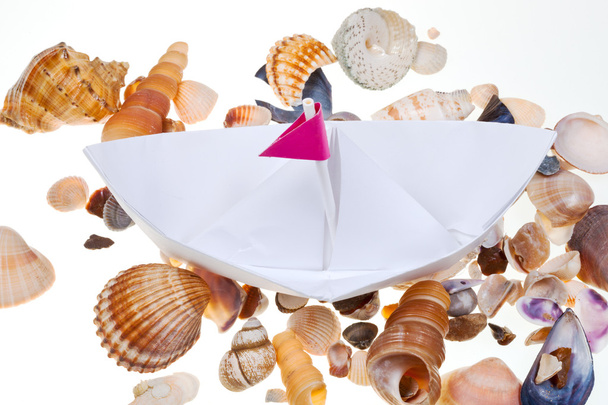 Barco de papel sobre fondo de conchas marinas
 - Foto, Imagen
