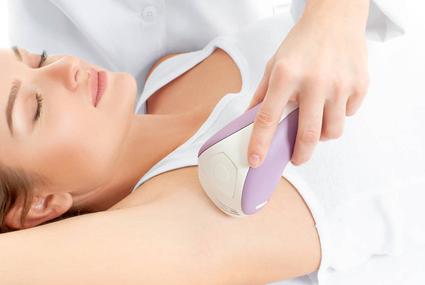 Beautician giving epilation laser treatment to woman on underarm - Фото, изображение