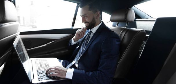 Businessman typing text on laptop while sitting in car - 写真・画像