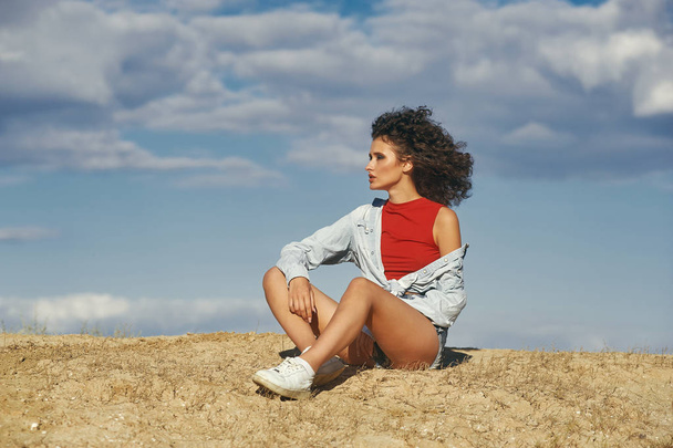 giovane ragazza seduta sulla sabbia di profilo contro il cielo, una giovane donna che respira aria fresca
. - Foto, immagini