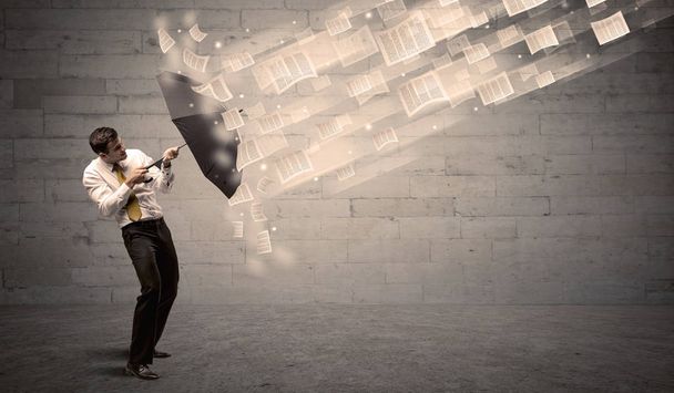 Business man protecting with umbrella against wind of papers - 写真・画像
