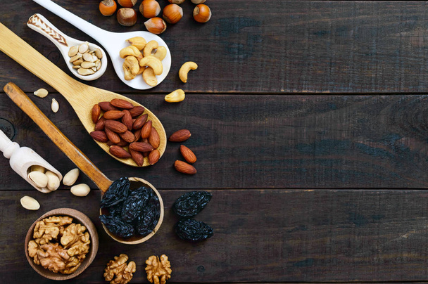 Assorted different nuts, prunes, pumpkin seeds in spoons on a dark wooden background. Top view. - Foto, imagen