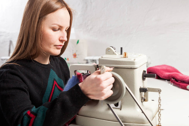 Молодая женщина скуднее, пушистый пристально смотрит и шьет яркий мех из натурального синего меха на швейной машинке
 - Фото, изображение