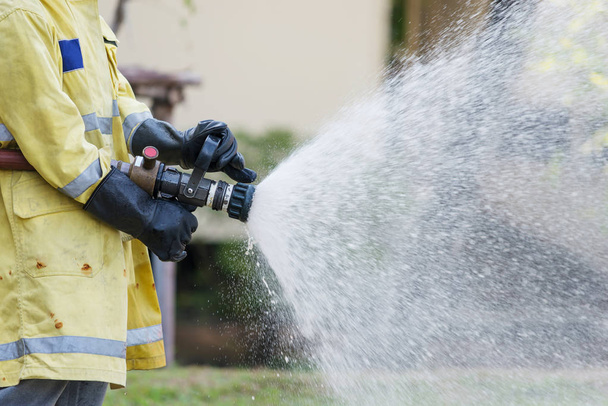 Firefighter holding high pressure fire hose nozzle. Firefighters training. - Water jet splashing - Photo, image