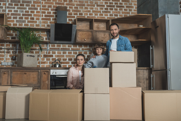 happy family with stacks of boxes smiling at camera while moving home - Photo, image