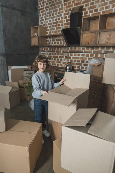 cute little boy smiling at camera while packing boxes during relocation - Φωτογραφία, εικόνα
