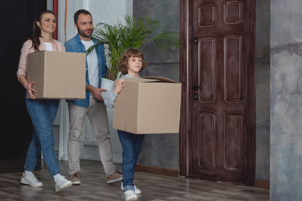 onnellinen perhe pahvilaatikoilla ja ruukkutehtaalla muuttamassa kotiin
 - Valokuva, kuva