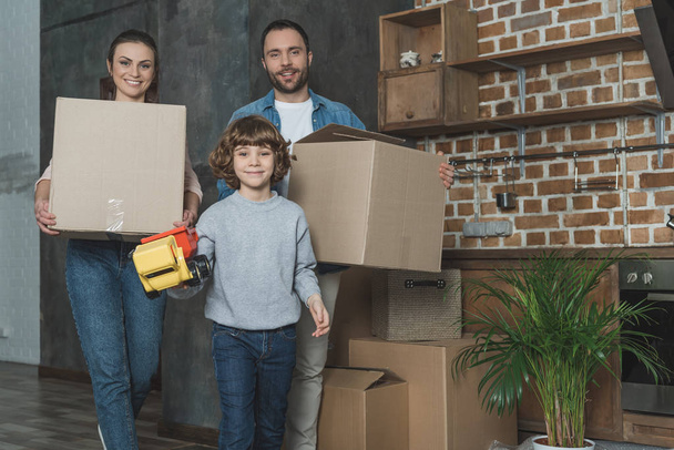 счастливая семья, держа коробки и игрушки, улыбаясь на камеру во время переезда
 - Фото, изображение