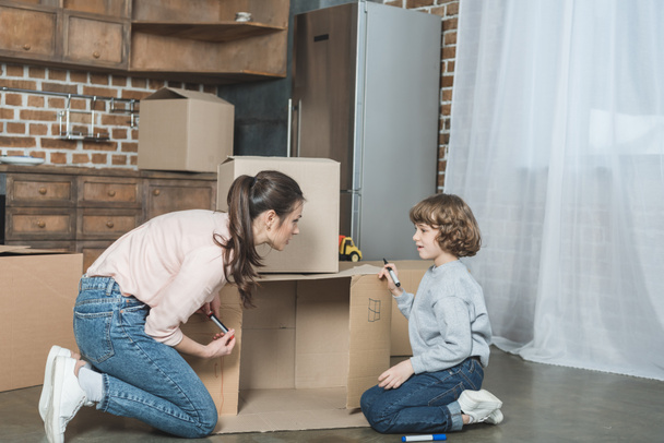 side view of mother and son drawing on cardboard box in new apartment  - Photo, Image