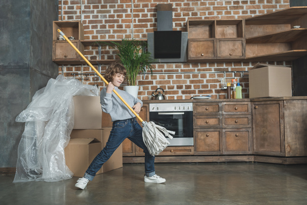 schattig gelukkig jongetje spelen met mop in nieuw huis - Foto, afbeelding