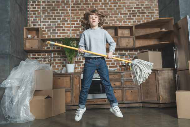 happy little boy jumping with mop in new house - Foto, Imagen