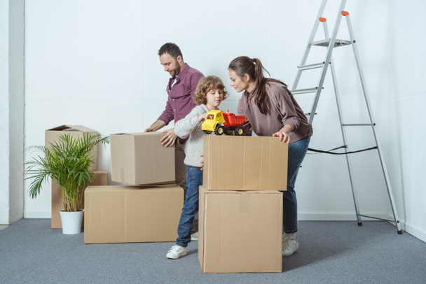 family with one kid packing cardboard boxes while moving home  - Φωτογραφία, εικόνα