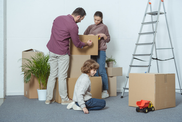 rodzice pakującą pudełka i syn grając na podłodze podczas relokacji - Zdjęcie, obraz