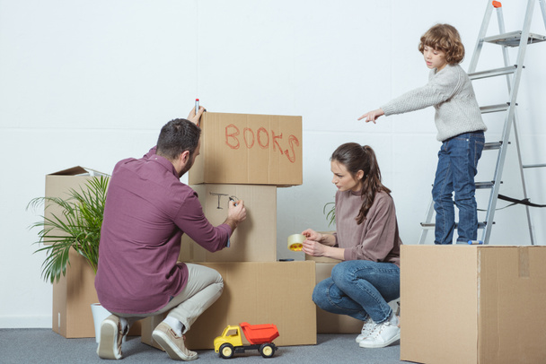 szülők csomagolási dobozok és fia mutató ujjával áthelyezés során - Fotó, kép