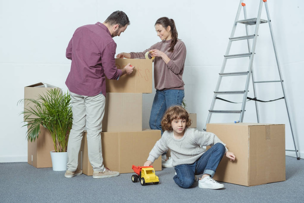 parents packing boxes and son playing with toy car during relocation - Photo, Image