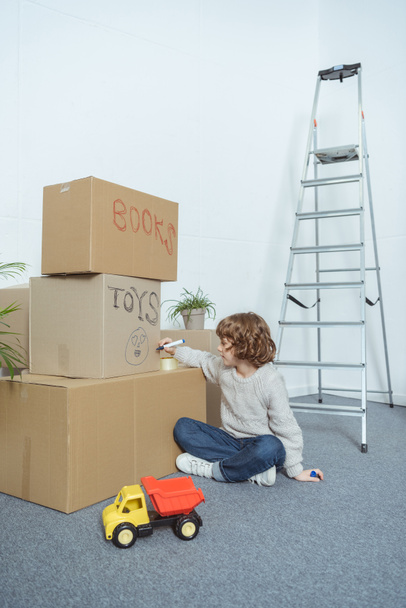 χαριτωμένο μικρό αγόρι τραγούδι κουτιά από χαρτόνι, ενώ κινείται σπίτι - Φωτογραφία, εικόνα