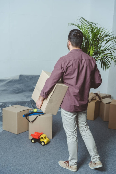 back view of man holding cardboard box while moving in new house - Photo, Image